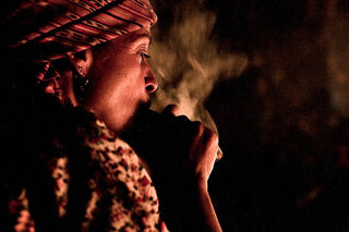 Person wearing a traditional Mayan headdress smoking a cigar in a dark setting