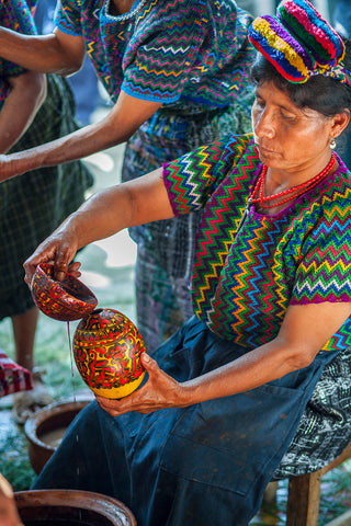 Mayan woman from Rabinal in traditional attire pouring cacao from a decorated container.