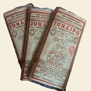 Three JUNAJPU cacao bars on a striped fabric background